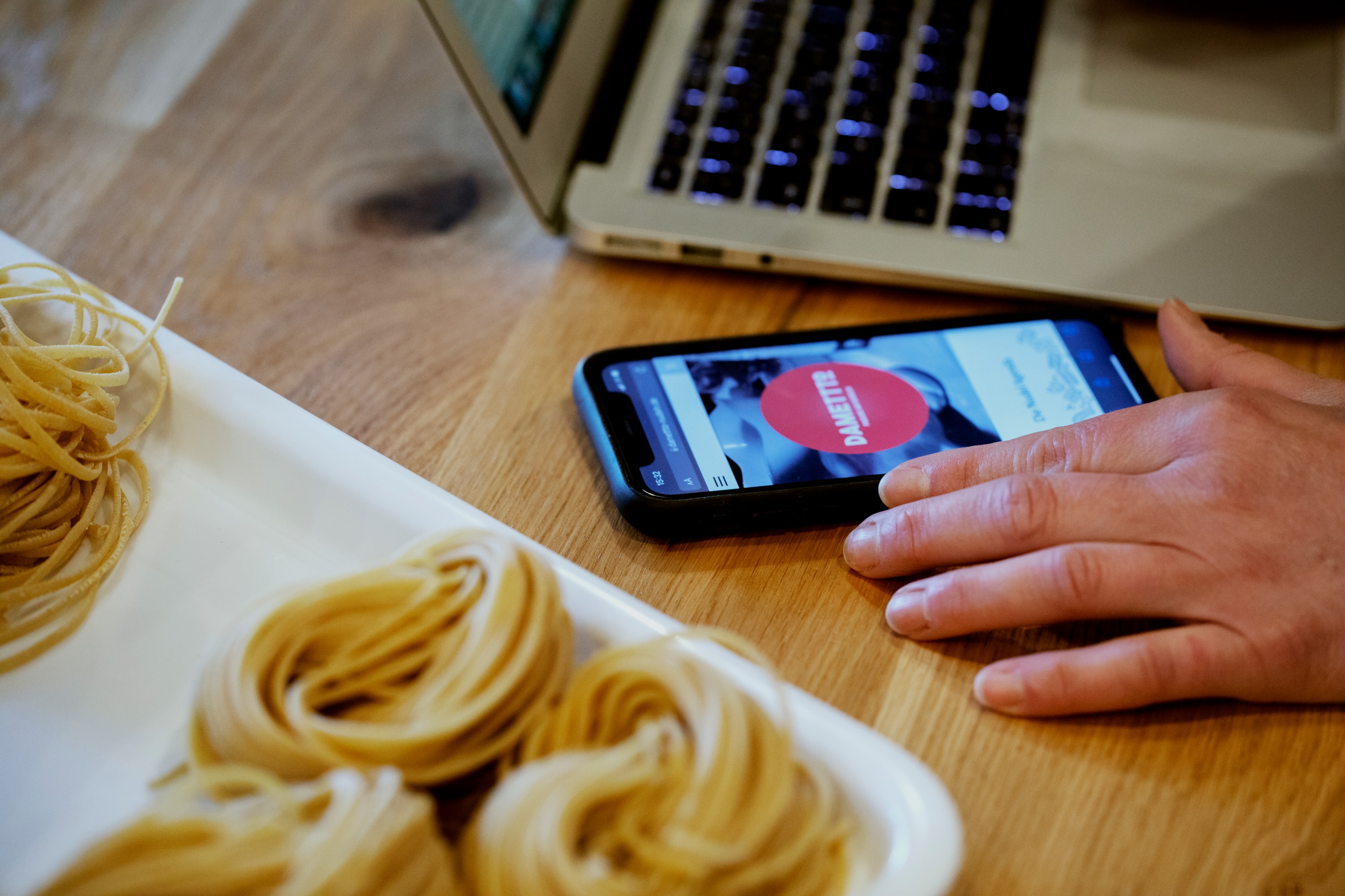 Selbstständige Unternehmerin Monica arbeitet mit Smartphone und Laptop an der Online-Präsenz ihrer Pastamanufaktur.