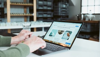 Person arbeitet am Laptop an einer Jimdo-Website. Im Hintergrund stehen Regale mit Gläsern und Kisten in einem hellen Atelier oder Büro.